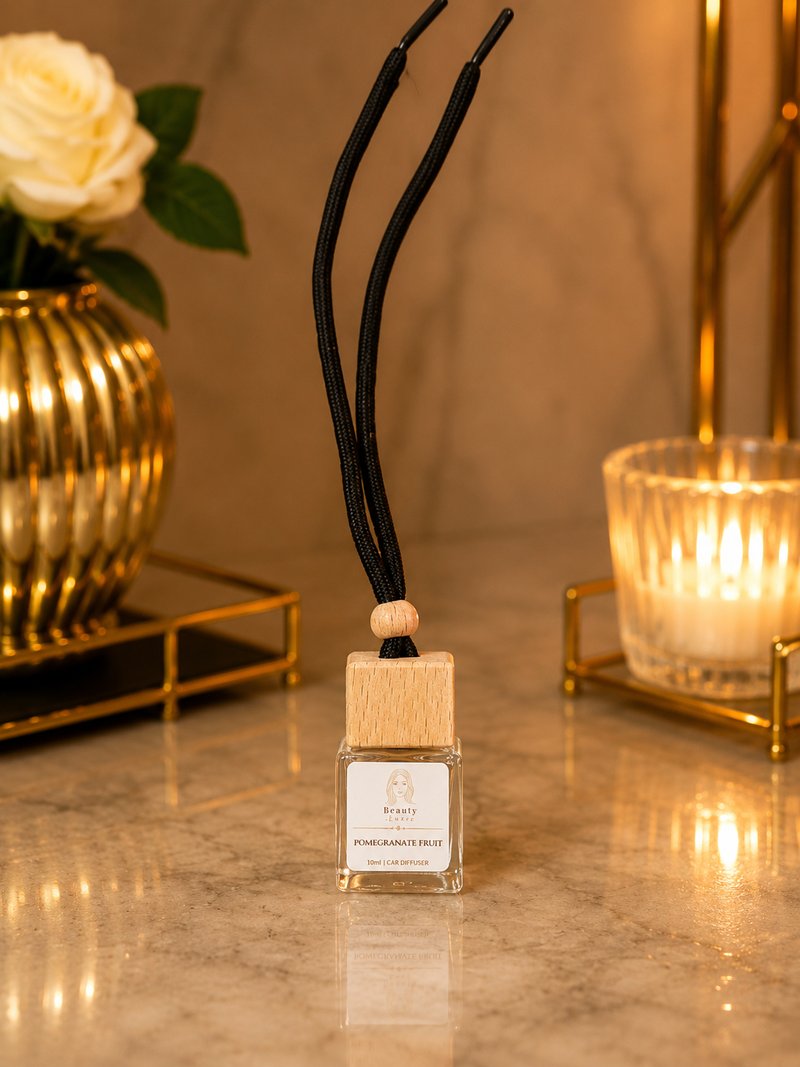 A Beauty Luxe car diffuser with a wooden cap and black cord, beside white roses and candlelight.