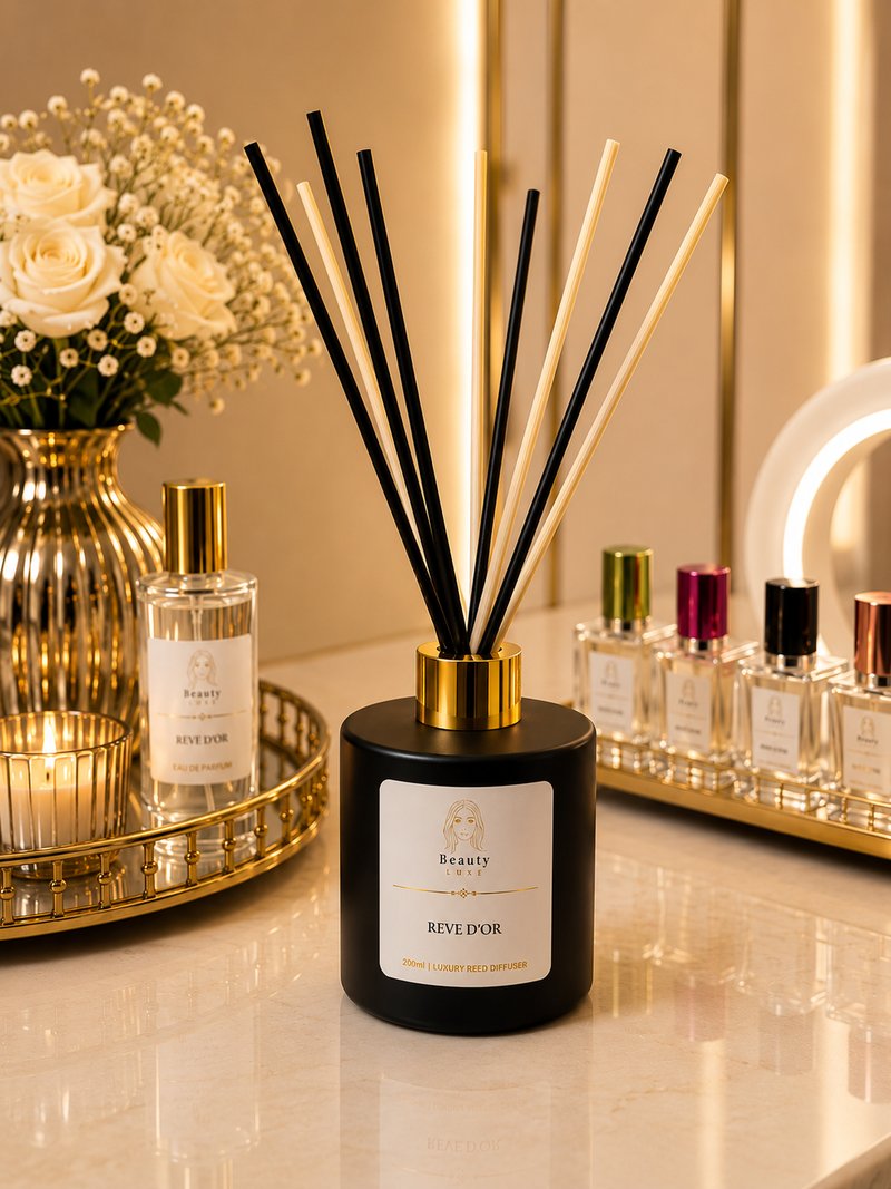 A Beauty Luxe reed diffuser with mixed black and natural reeds, beside white roses and candlelight.